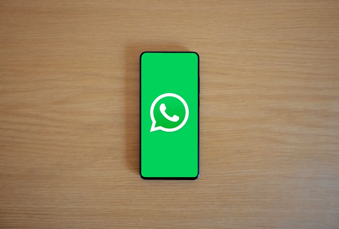 Top view of smartphone displaying WhatsApp logo on a wooden background, represen