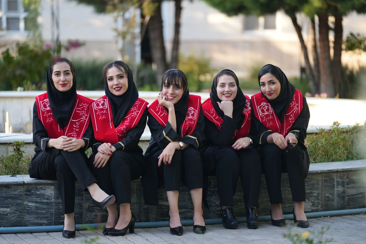 Five Iranian women in graduation attire, smiling outdoors, celebrate their achie