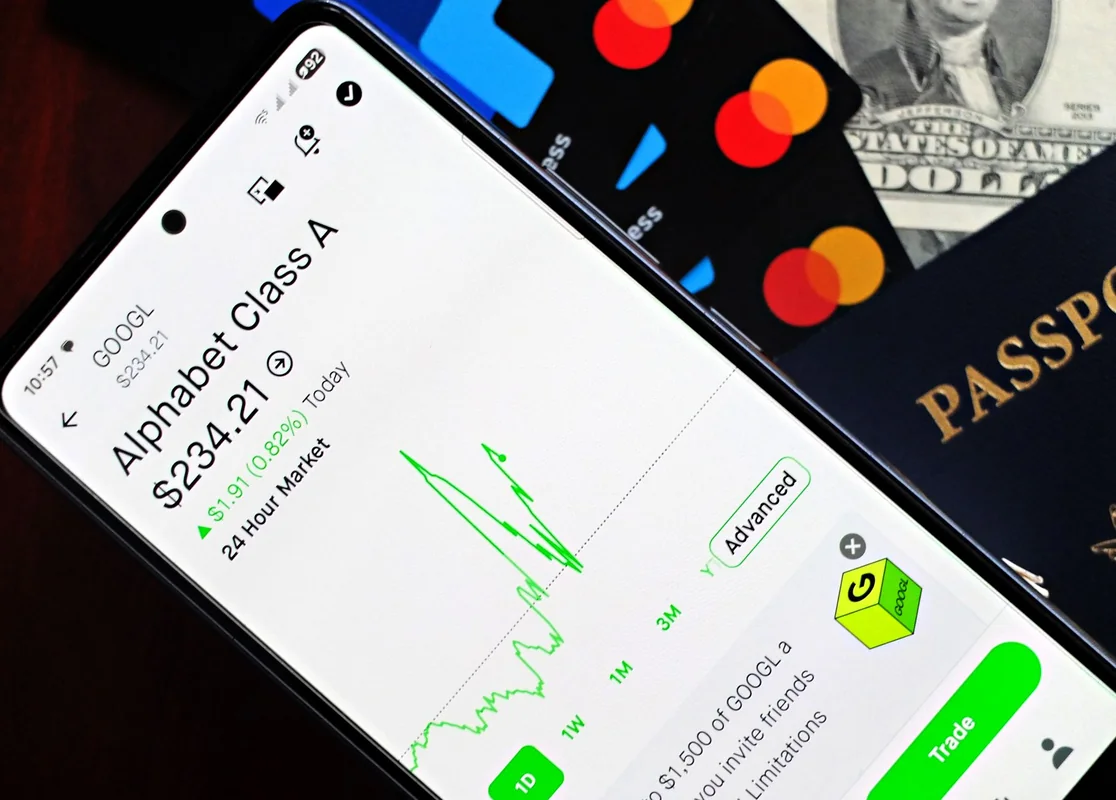 Smartphone displaying stock market app next to U.S. dollar and passport, represe
