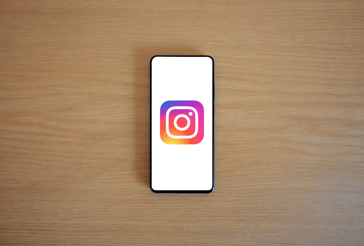 A smartphone with the Instagram logo on display, placed on a wooden surface. Per