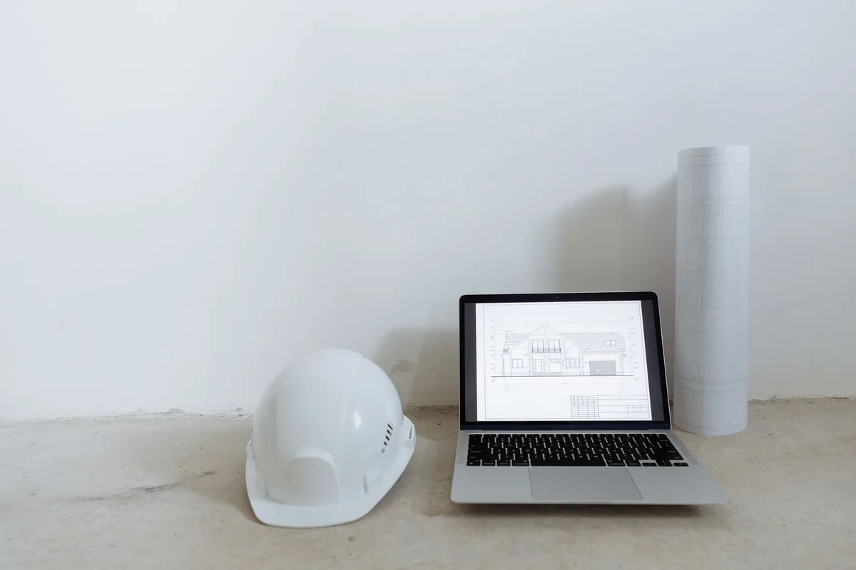 A clean workspace with laptop, hard hat, and blueprints for construction plannin