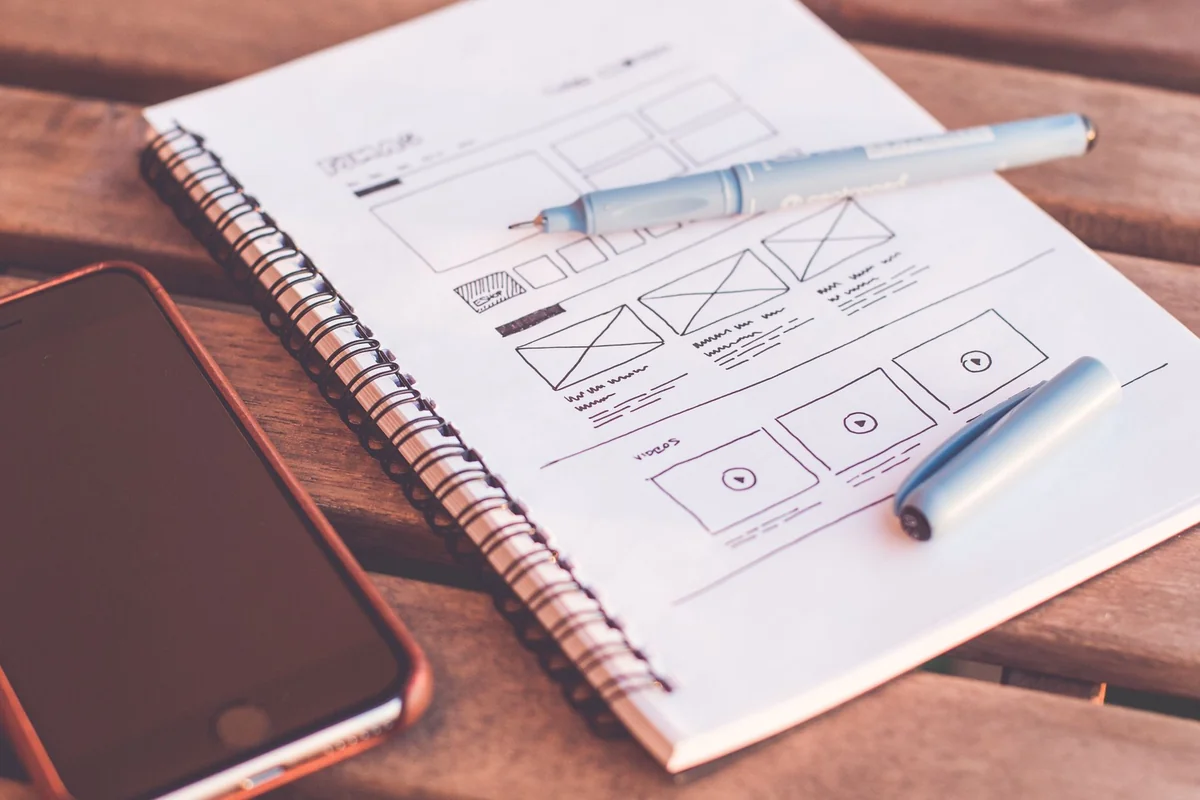 Close-up of a notebook with wireframe sketches and a smartphone on a wooden desk